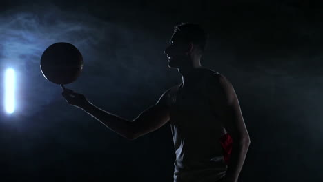 Close-footage-of-basketball-player-spinning-ball-on-his-finger,-dark-misty-room-with-floodlight